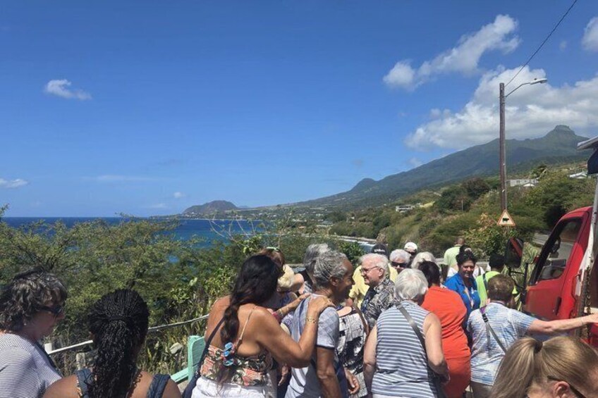 A group of people gathered on a hillside overlooking a coastal landscape with mountains in the distance. 1