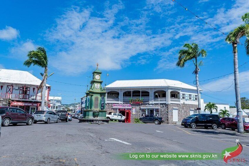 A street with cars, a clock tower, and palm trees. 4