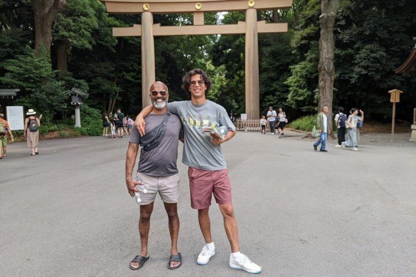 Two people standing in front of a large gate with a tree-lined background. 2