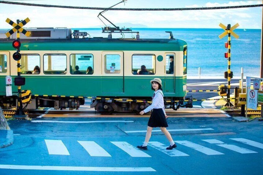 A green tram at a railway crossing with a pedestrian crossing and a coastal background. 1