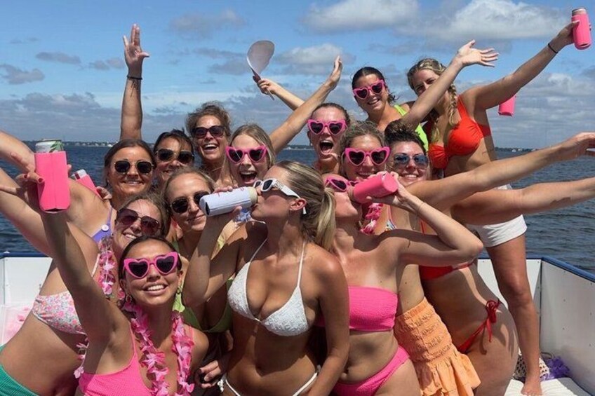 A group of people on a boat, wearing swimsuits, with some holding pink foam cups. 3