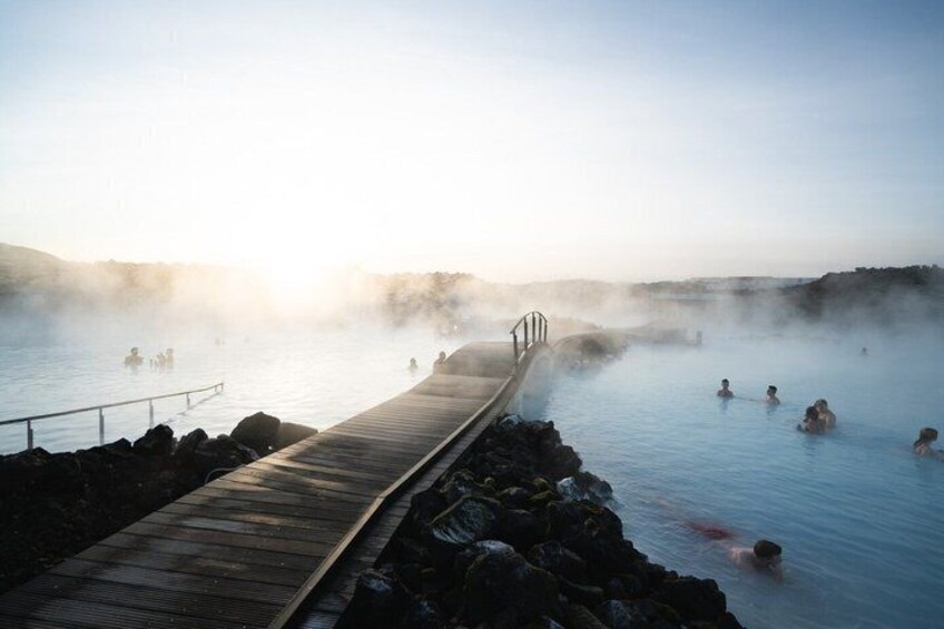 A wooden boardwalk leading to a geothermal spa with people in the water. 4