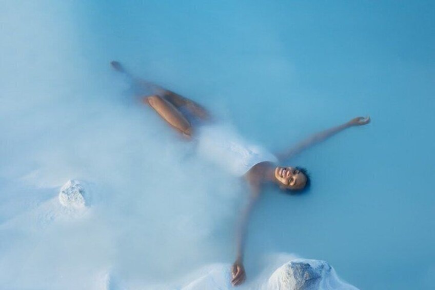 A person floating in a clear blue pool with steam rising from the water. 2