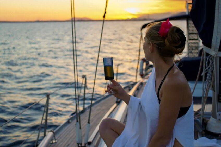 Une personne assise sur le pont d’un bateau au coucher du soleil, tenant un verre à la main. 1