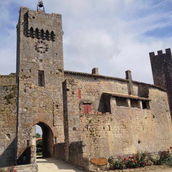 A historic stone building with a tower, arched entrance, and a sign indicating access for vehicles. 1
