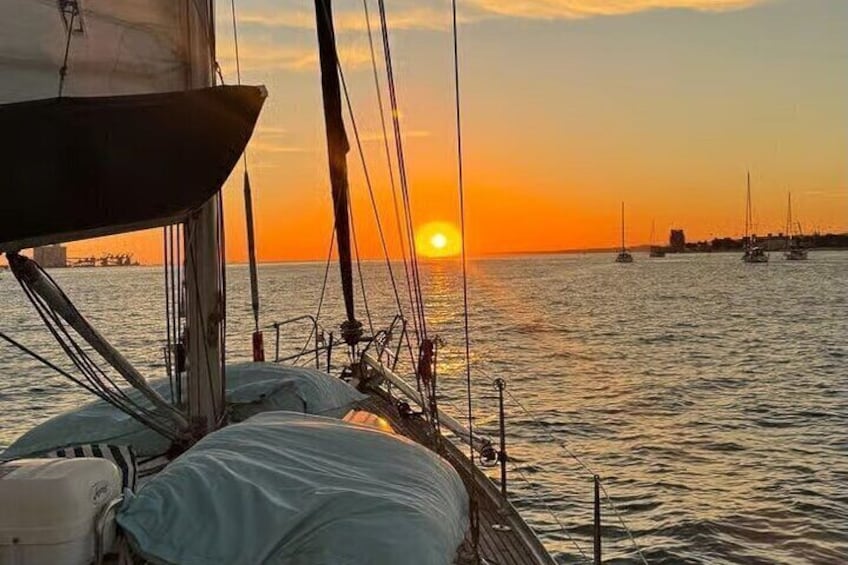 A sailboat at sunset with the sun setting on the horizon and other boats in the distance. 1