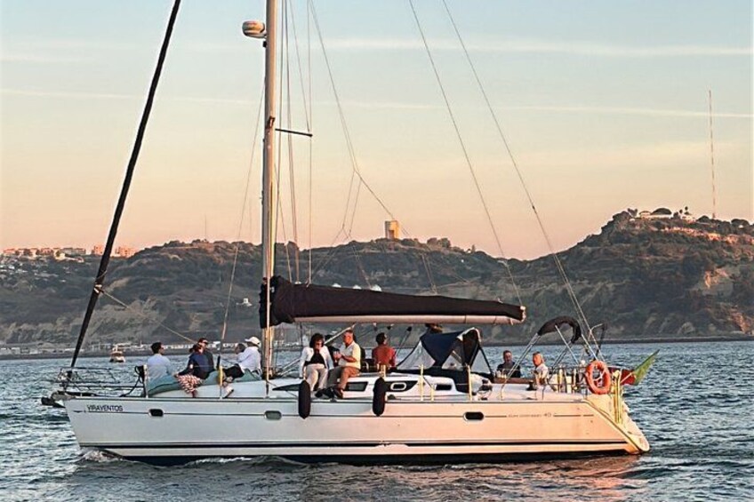 Una barca a vela con persone a bordo, una costa rocciosa e un faro sullo sfondo. 2