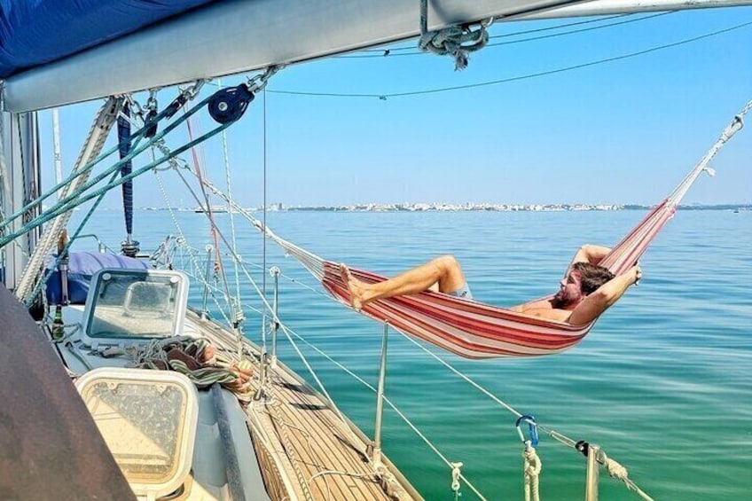 A person relaxing in a hammock on a boat, with calm water and a distant shoreline in the background. 2
