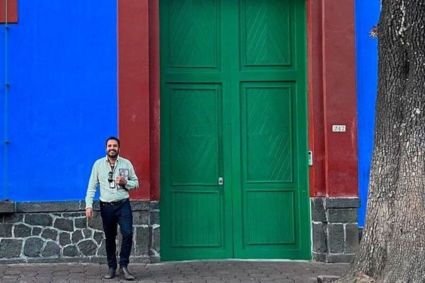 Una persona de pie frente a una puerta verde con un muro azul y rojo. 1