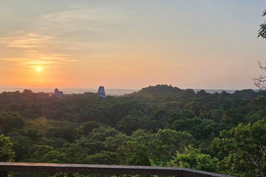 Un atardecer sobre un paisaje boscoso con una colina distante y una pequeña estructura. 2