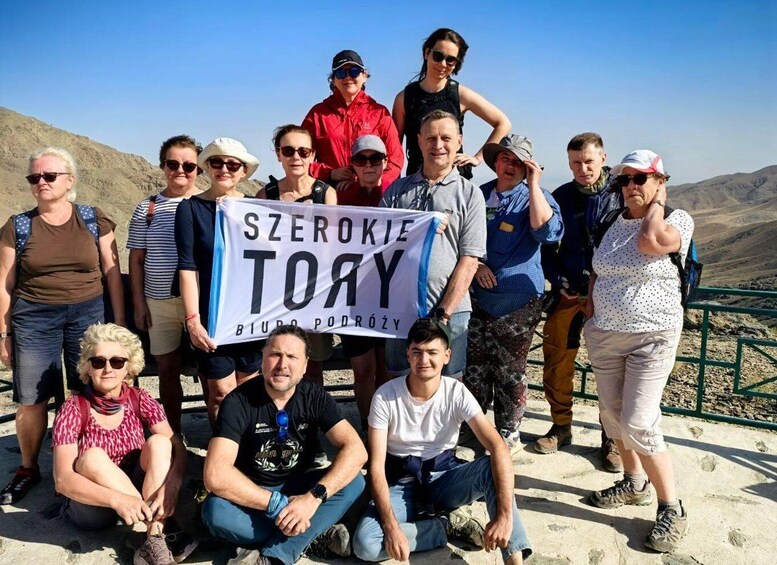 A group of people standing on a rocky outcrop with a banner reading 'Szerokie Tory' and 'Biuro Podróży'. 3