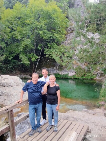 Three people standing on a wooden platform by a clear water body surrounded by greenery and rocks. 2