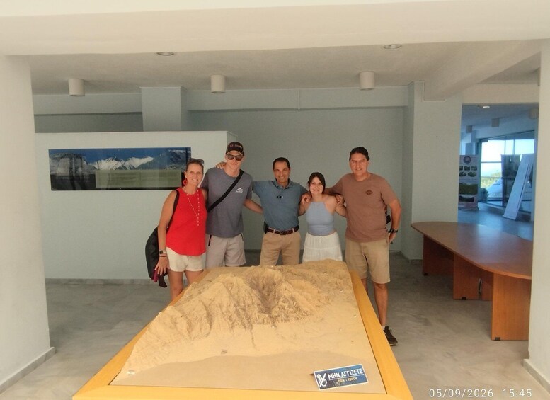 A group of people standing in a room with a large sand mound and a sign that reads 'MNH ATTITETE DON'T TOUCH'. 3