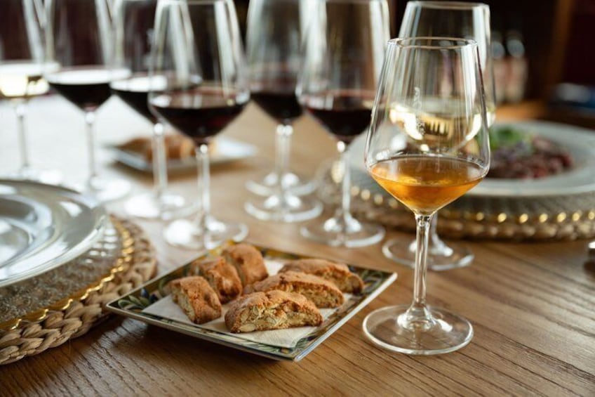 A wooden table with a plate of pastries, a glass of white wine, and several glasses of red wine. 4