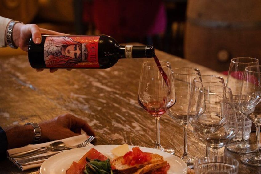 A person pouring red wine into a glass from a bottle with a label. 1