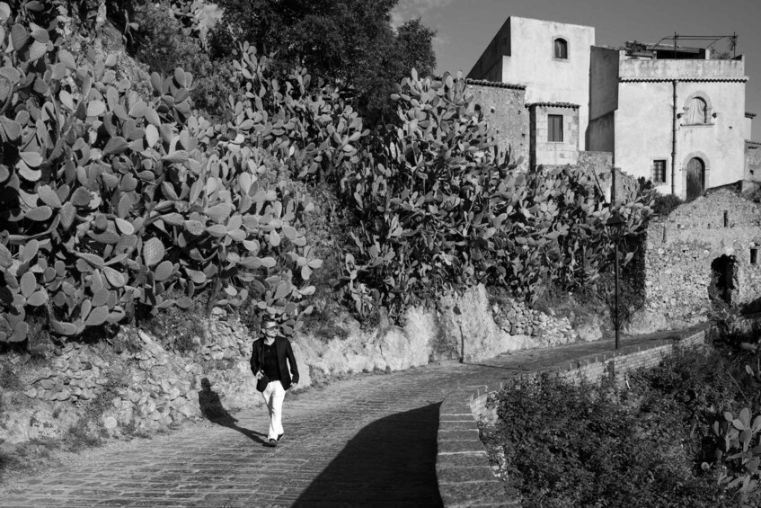 A cobblestone path, a person walking, and a building with a stone wall and vegetation. 4