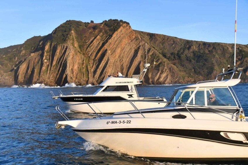 Two boats on calm water with a rocky cliff in the background. 1