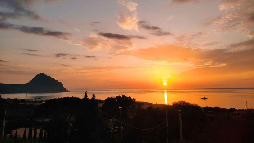 A sunset over a calm sea with a mountain silhouette and a boat in the distance. 1