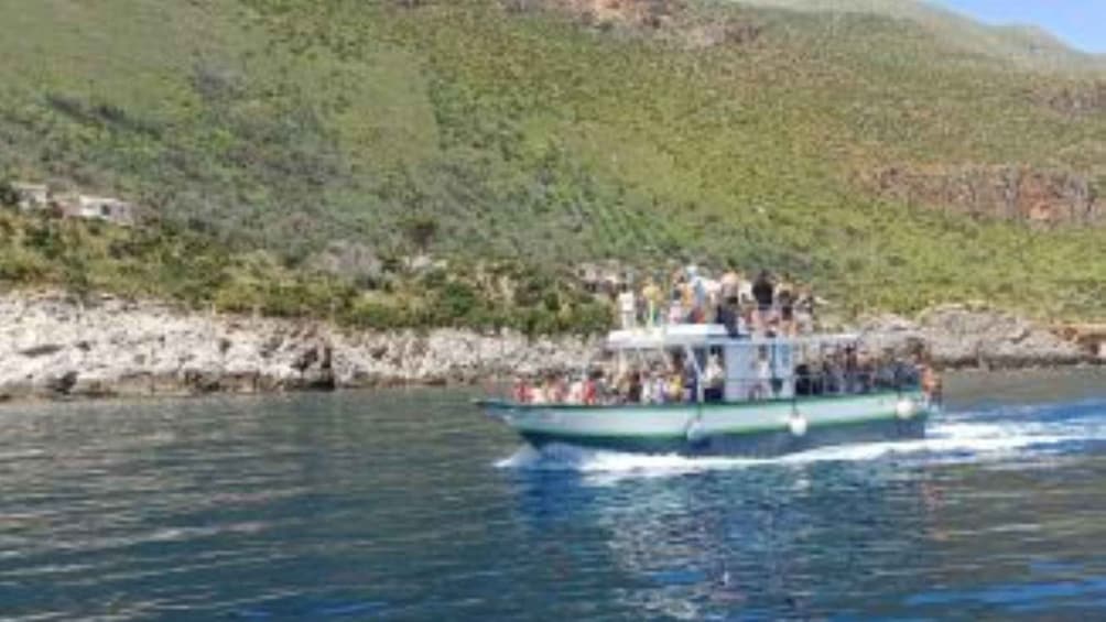 A boat with passengers on a body of water, surrounded by greenery and hills. 3