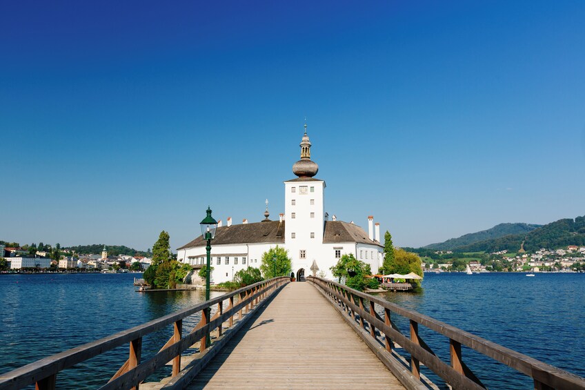 Eine hölzerne Brücke führt zu einem weißen Gebäude mit einem Turm am See. 2
