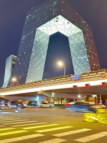 A modern building with a distinctive geometric design, a bridge with traffic lights, and a street with vehicles. 3