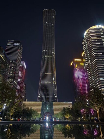 A tall skyscraper with a unique cylindrical shape, surrounded by other high-rise buildings with illuminated windows. 4