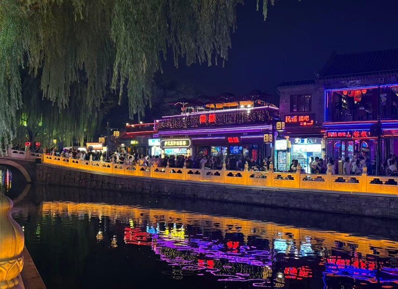 A riverside walkway with illuminated buildings and reflections on the water. 4