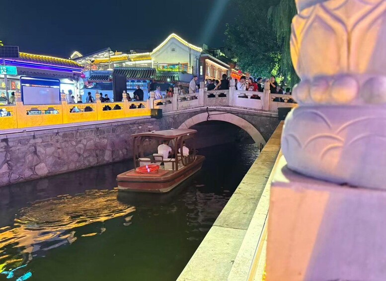 A traditional Chinese waterway with a boat, a stone bridge, and illuminated buildings. 5
