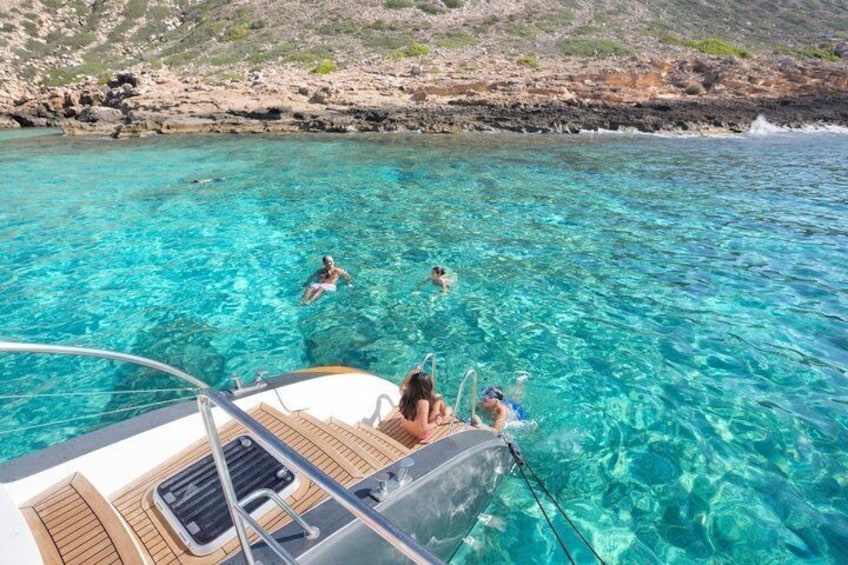 A clear blue sea, a boat with people on board, and rocky coastline. 1