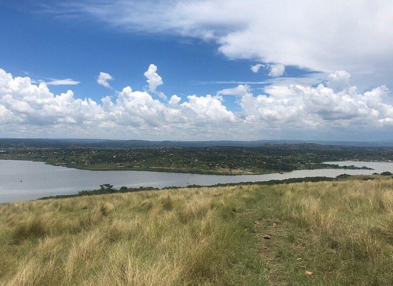 A grassy hilltop with a view of a lake and a distant town. 3