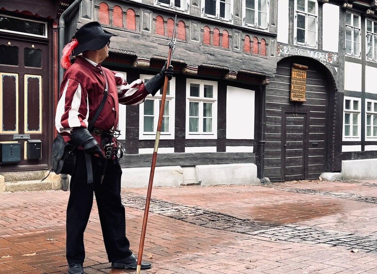 A uniformed individual standing on a brick pavement, holding a long pole, with a traditional building in the background. 4
