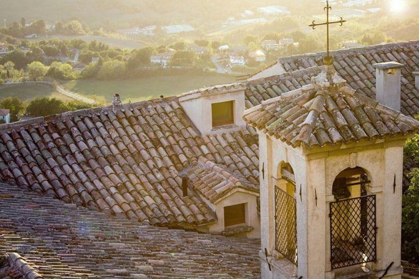 A village with terracotta-tiled roofs, a small tower with a gate, and a river in the background. 4