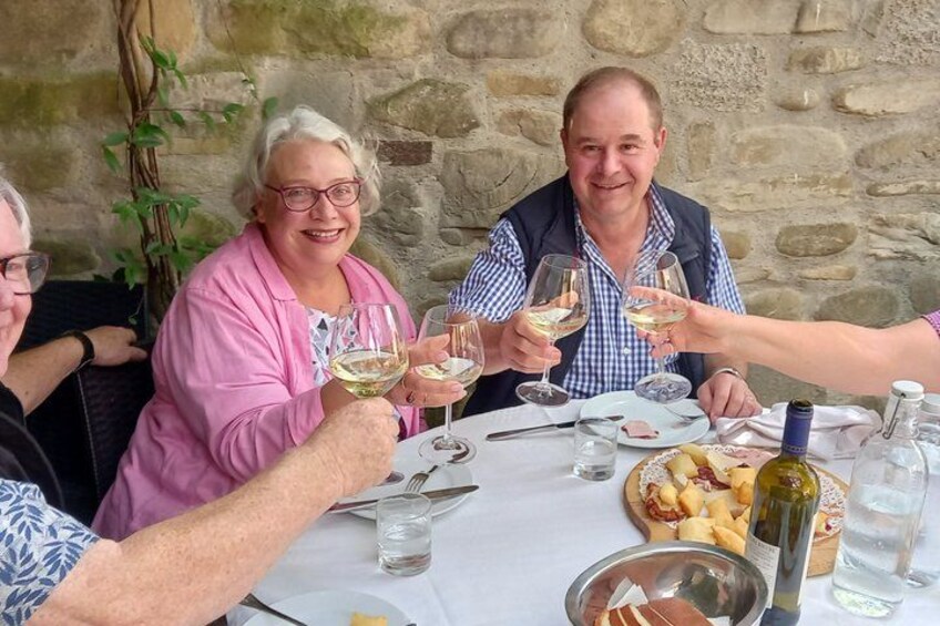Un grupo de personas brindando con copas de vino en una mesa con comida y una botella de vino. 4