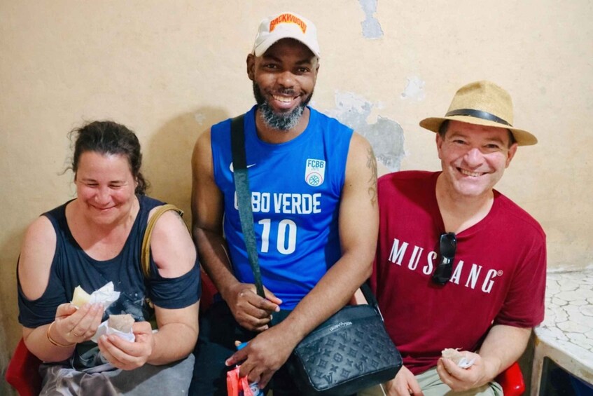 Drei Personen sitzen zusammen, eine trägt ein blaues Trikot mit der Nummer 10, eine andere ein rotes Hemd und die dritte ein schwarzes Tanktop. 1