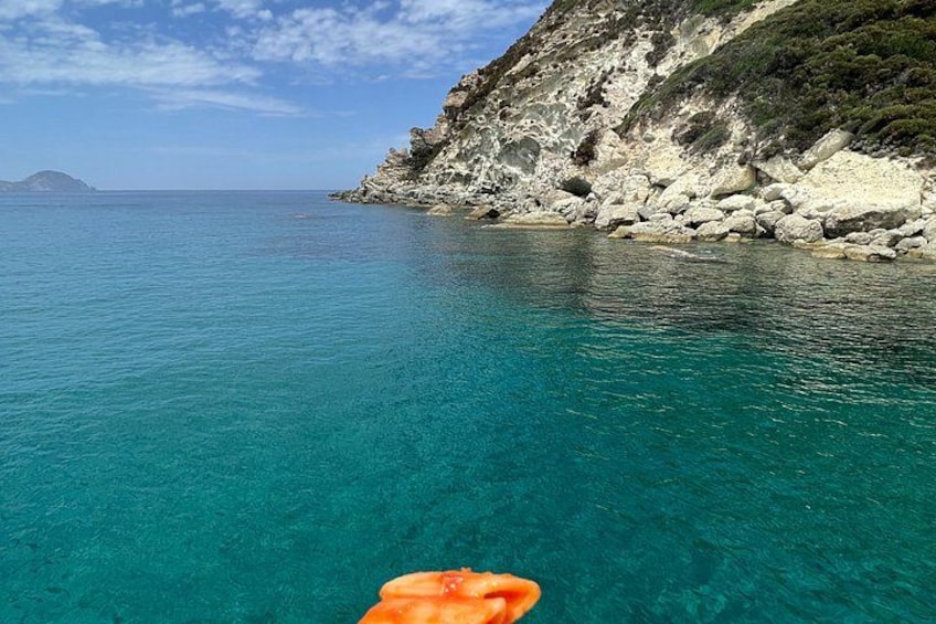 A coastal landscape with clear turquoise water, rocky cliffs, and a distant island. 5