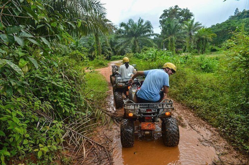 Twee personen rijden op quadbikes over een modderige pad in een tropisch regenwoud. 5