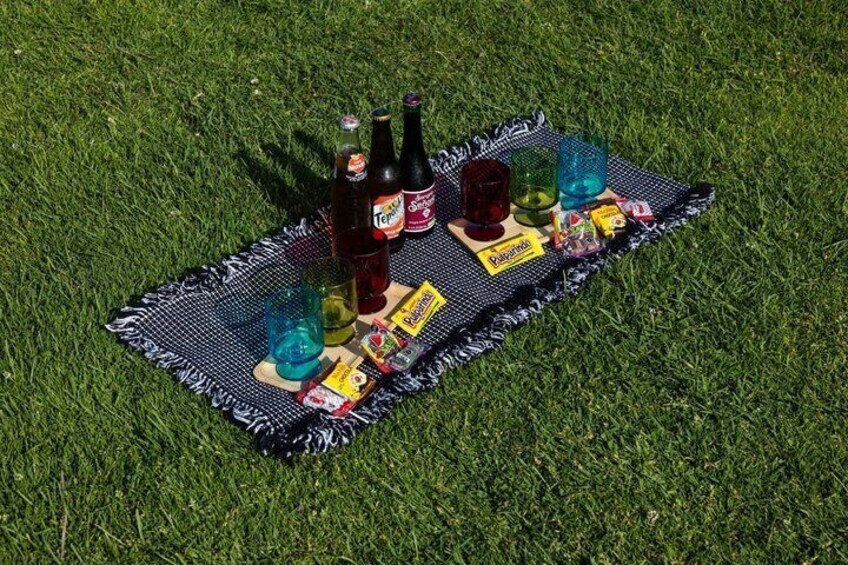Un pique-nique installé sur un champ herbeux, avec une couverture, des bouteilles, des verres et des en-cas. 2