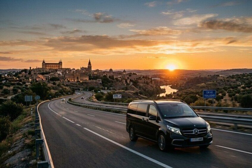 A black van driving on a highway with a sunset in the background and a sign for Toledo. 2