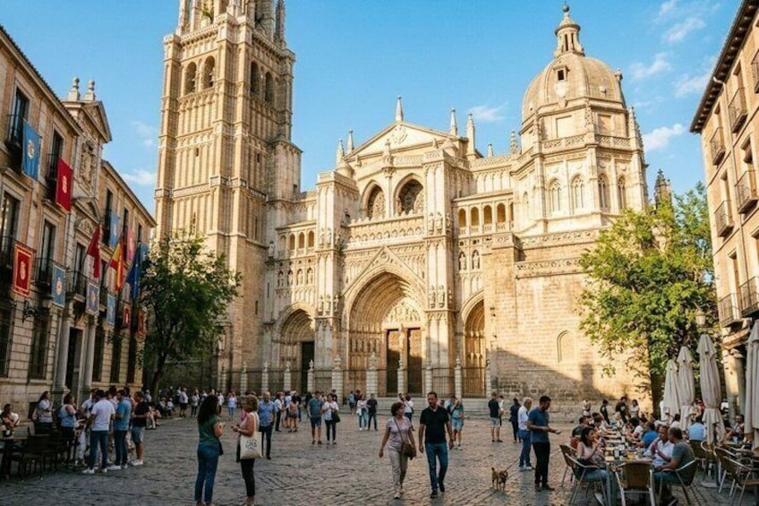 A historic cathedral with a tall bell tower, a large arched entrance, and a crowd of people in a cobblestone square. 1