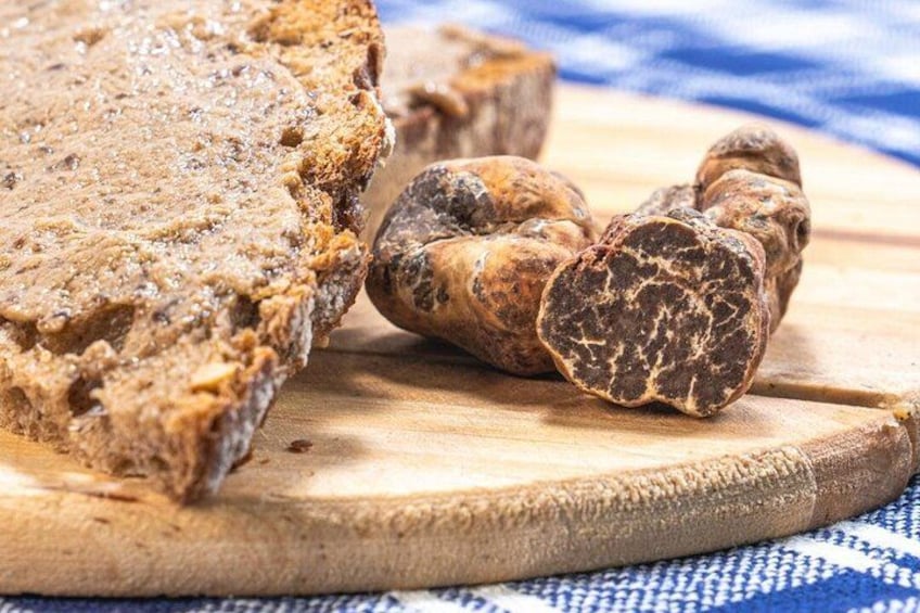 A loaf of bread and a cut piece of cured meat on a wooden cutting board. 2