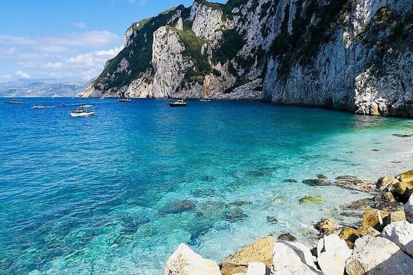 A coastal scene with clear blue water, rocky shore, and boats. 5