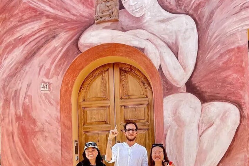 Eine große Holztür mit einer Statue darüber, vor einer rosafarbenen Wand. 5