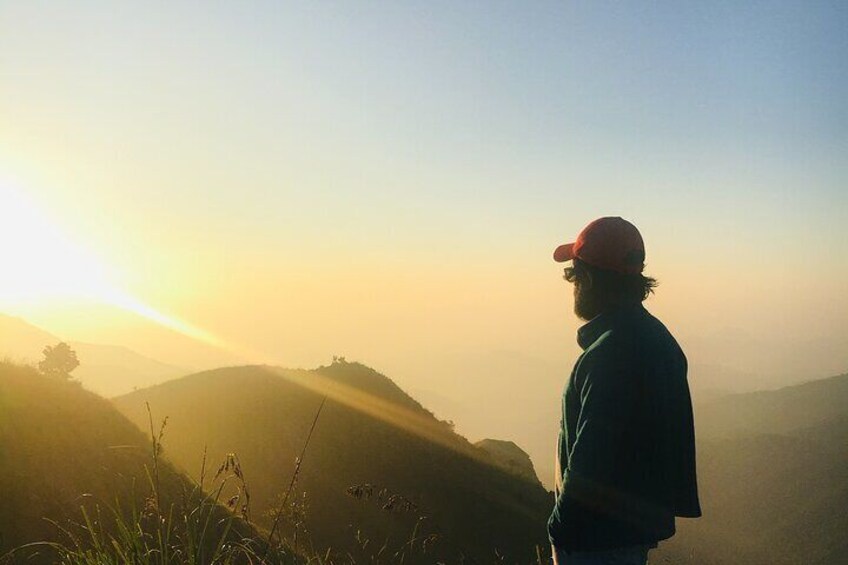 A person standing on a hill during sunrise with misty hills in the background. 5