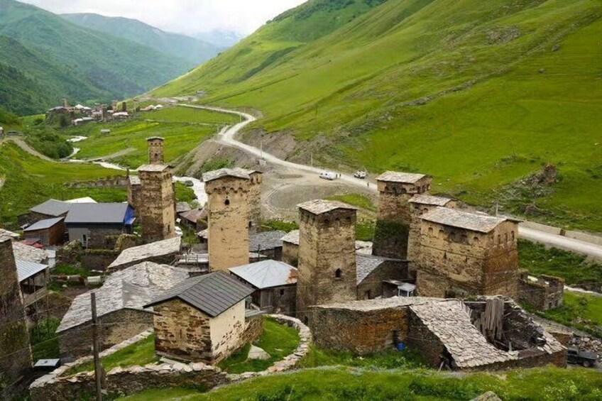 A medieval castle complex with towers, surrounded by lush green hills and a winding road. 5