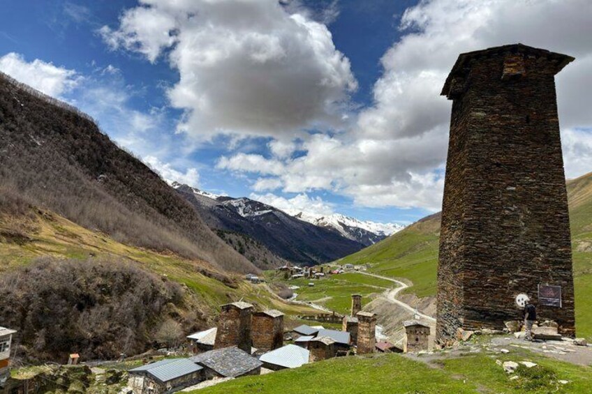 A village with stone buildings, a tall tower, and mountains in the background. 4