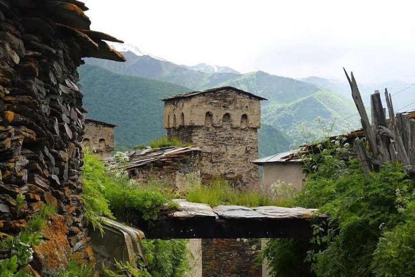A stone structure with a bell tower, surrounded by lush greenery and mountains in the background. 1