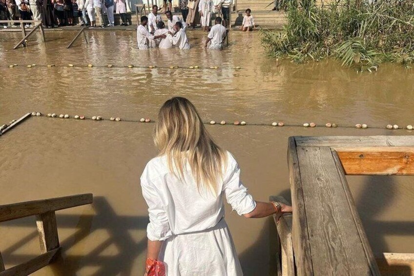 Una persona con un vestido blanco de pie junto a una baranda de madera, mirando a un grupo de personas en una zona de aguas poco profundas con objetos flotando. 3