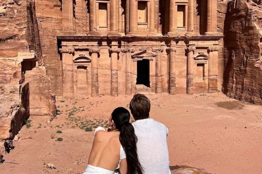 Un couple se tient devant une grande structure en grès, ornée de colonnes et dotée d’une porte d’entrée. 5