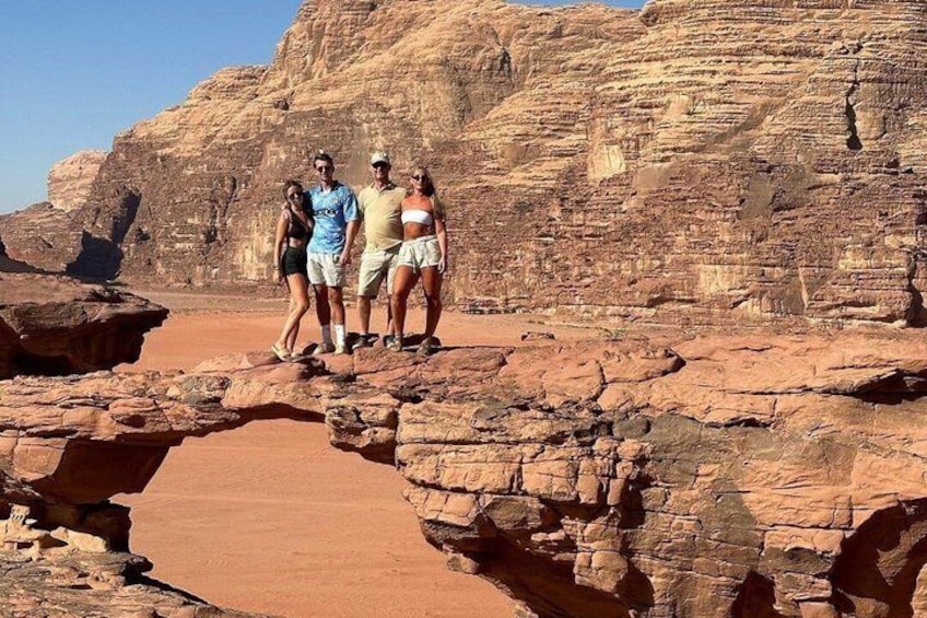 Un groupe de personnes se tient sur une formation rocheuse, avec un pont naturel en premier plan. 4