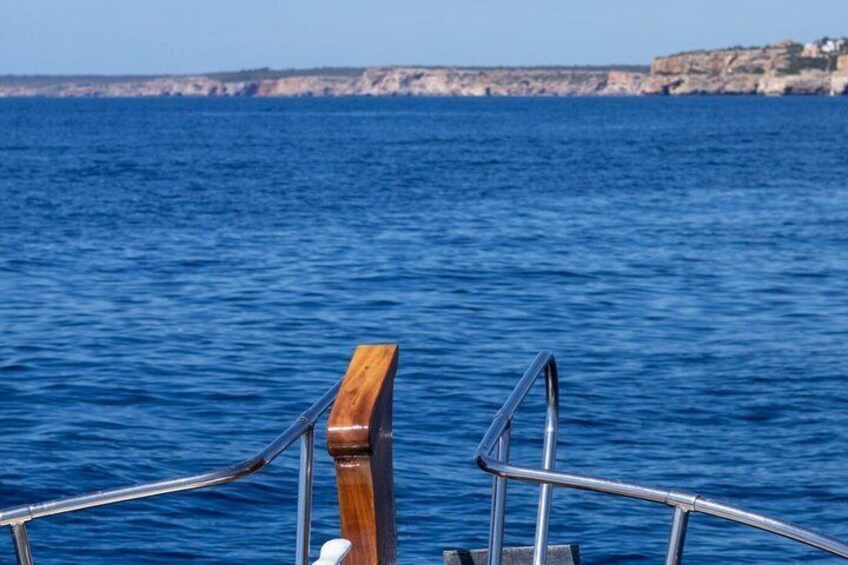 Una ringhiera di legno su una barca, con vista sul mare e sulle scogliere sullo sfondo. 4